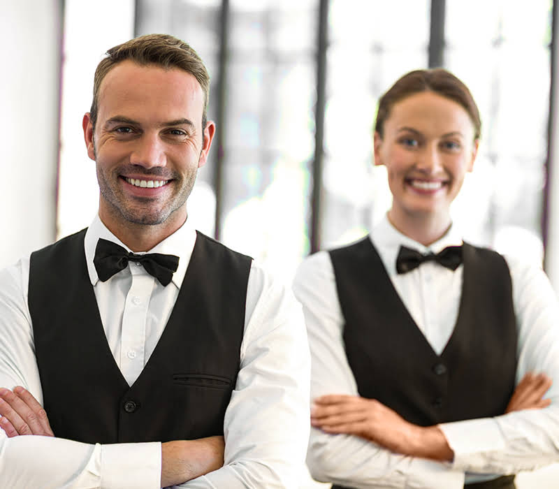 Das Dreiburgensee – Jobs Hero (Mob) Das Dreiburgensee - Jobs & Karriere: zwei Chefs de Rang in weißem Hemd und schwarzem Gilet mit schwarzer Fliege lächeln in die Kamera